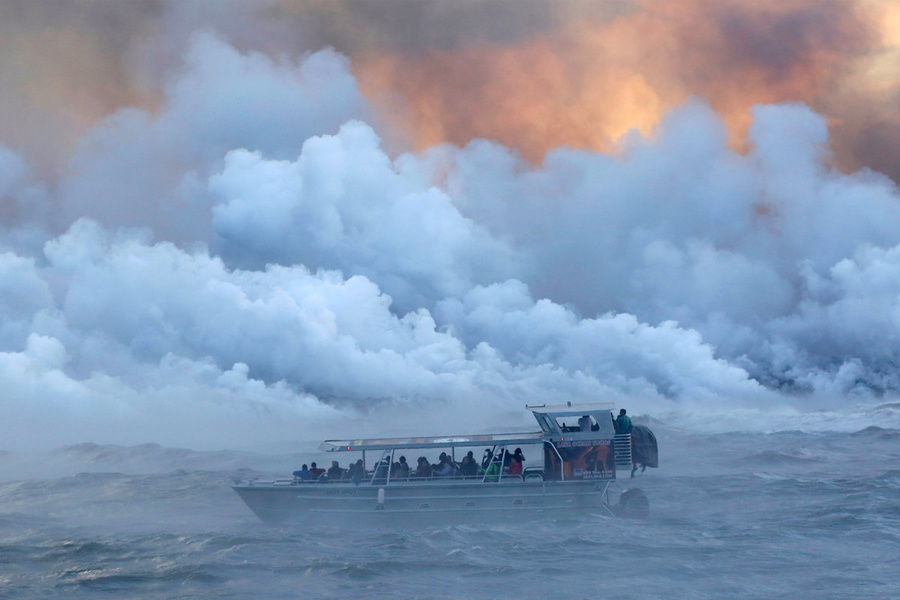Tourists watch the lava of Kilaua volcano erupt into the Pacific Ocean.